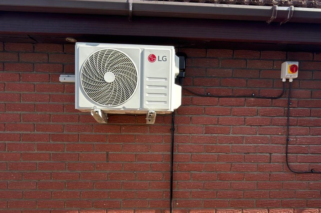 Outdoor air conditioning unit with its electrical isolator switch on a red brick wall