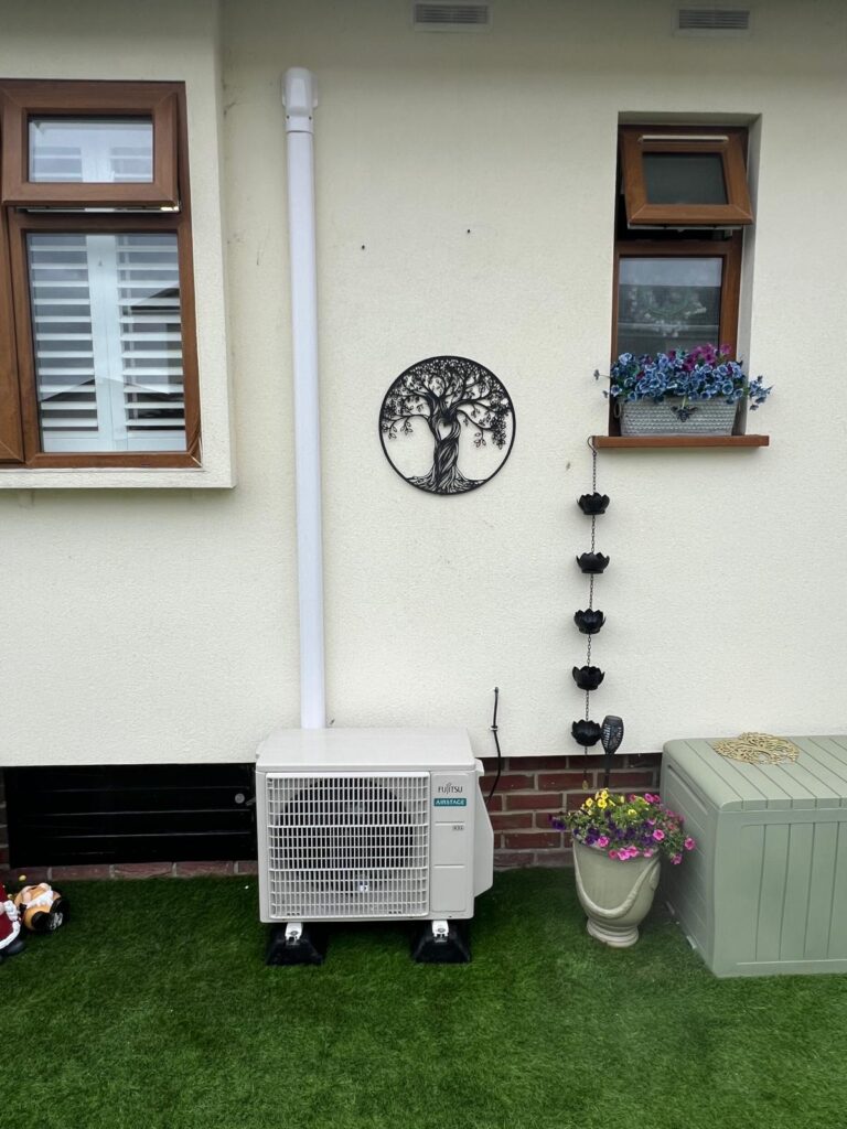 Outdoor air conditioning unit at ground level against a rendered garden wall