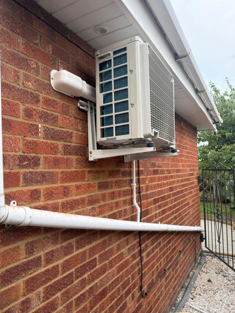 Outdoor air conditioning unit on a wall bracket under the eaves, with white pipe trunking